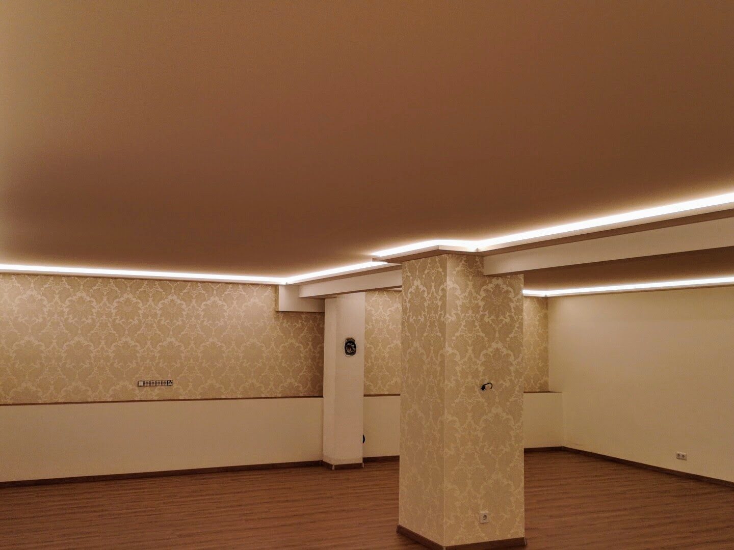Großer Raum mit Spanndecke und umlaufender Lichtvoute am Abend